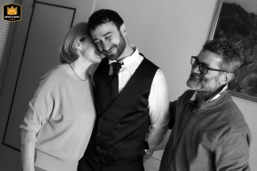 At the groom’s home in Gonzaga, Mantua, Italy, after a family portrait, his mother gently seeks a heartfelt connection with him. The groom appears visibly moved, captured in an intimate black-and-white image.